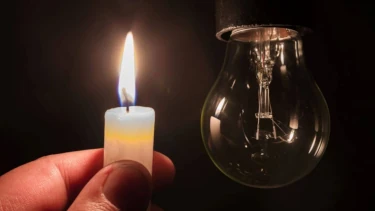 foto van een gedoofde elektrische lamp en daarnaast is een hand te zien die een brandende kaars vasthoudt