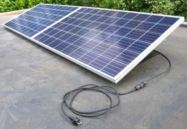 een foto waarop twee zonnepanelen te zien zijn die op een plat dak liggen en een elektriciteitssnoer waaraan een 230 Volt steker zit (die nog in het stopcontact gestoken moet worden)