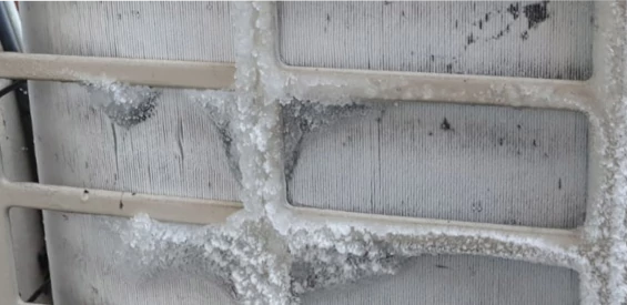detailopname van de metalen lamellen van de buitenunit.<br>Het is de rijp op de lamellen (achter grove traliewerk) die de doorstroming van de lucht bemoeilijken