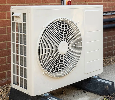 een buitenunit van een lucht-water warmtepomp met links (door het traliewerk zichtbaar) de dunne metalen lamellen van de verdamper