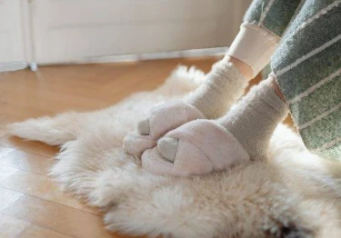 een dame die pantoffels aan haar voeten heeft en onder die pantoffels nog een deken om maar geen koude voeten te hebben